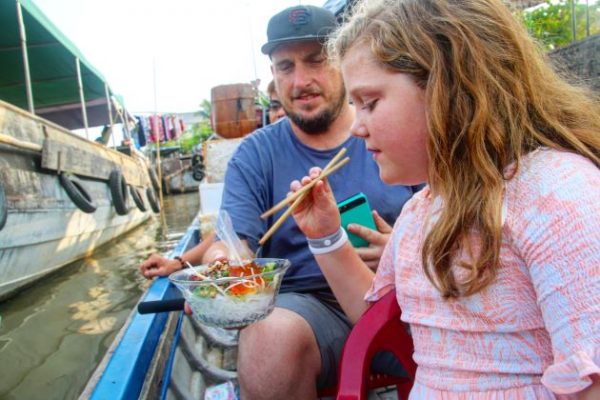 enjoy food on boat at a floating market in mekong delta on a family vacation in vietnam